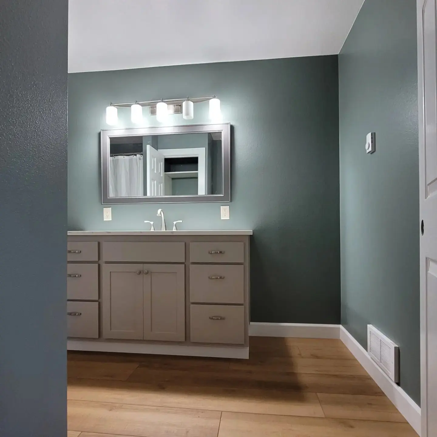 Single sink gray vanity with white marble countertop against a dark teal accent wall in Alfalfa.
