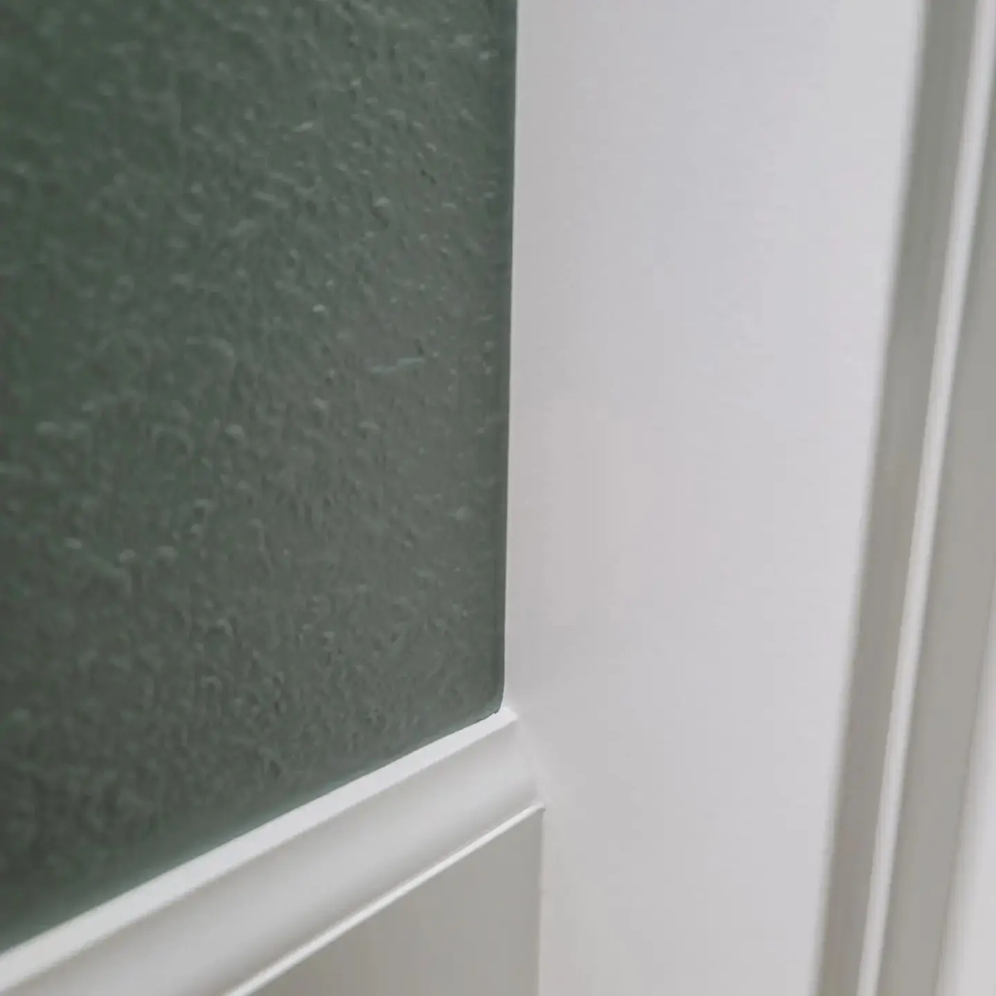Expertly cut-in paint lines showing the transition from white trim to a dark teal bathroom wall.