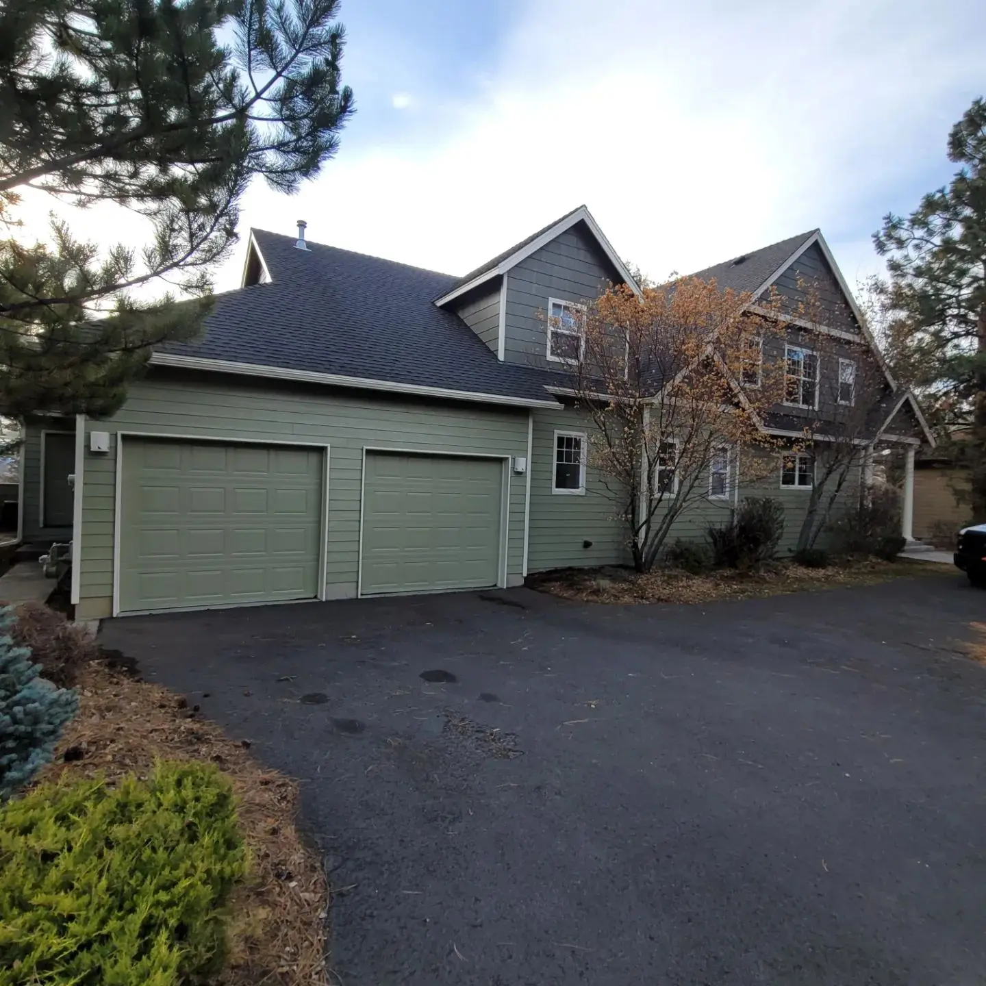 Two-car garage area in Bend OR featuring freshly painted sage green doors and slate blue shingle accents.