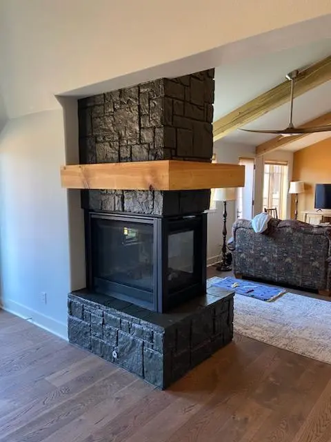 Professional black painted stone fireplace surround with a custom natural wood mantel in a Redmond home.