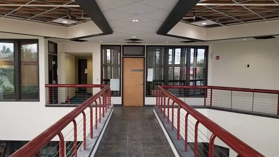 Interior view of an academy hallway featuring neutral walls, dark trim windows, and a red metal railing balcony