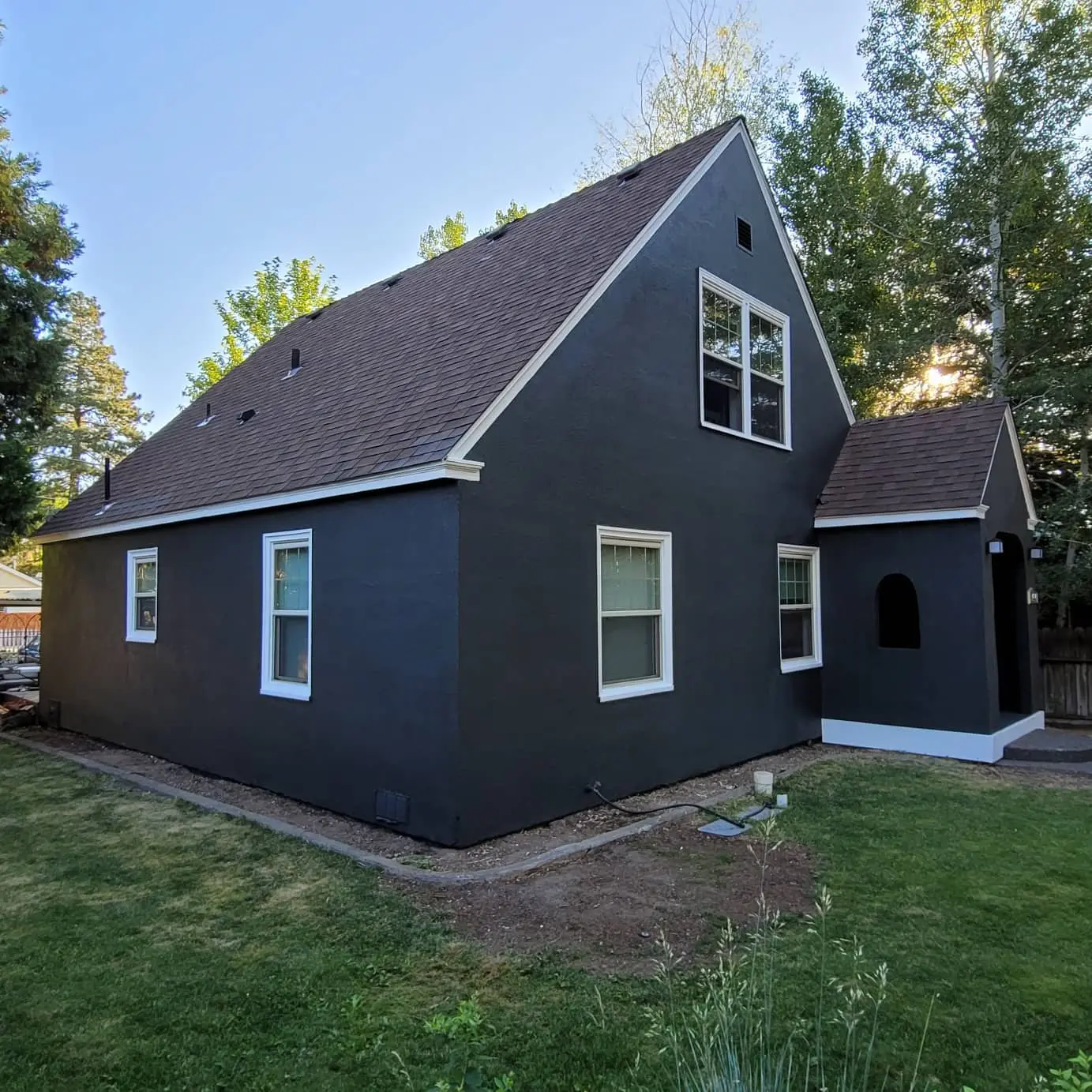 After view of the same side wall, now featuring a smooth, dark charcoal stucco finish with white-painted window trim.