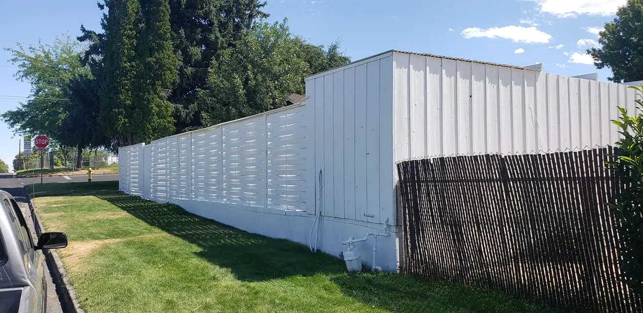 Street-side view of a white painted privacy fence and matching utility structure.