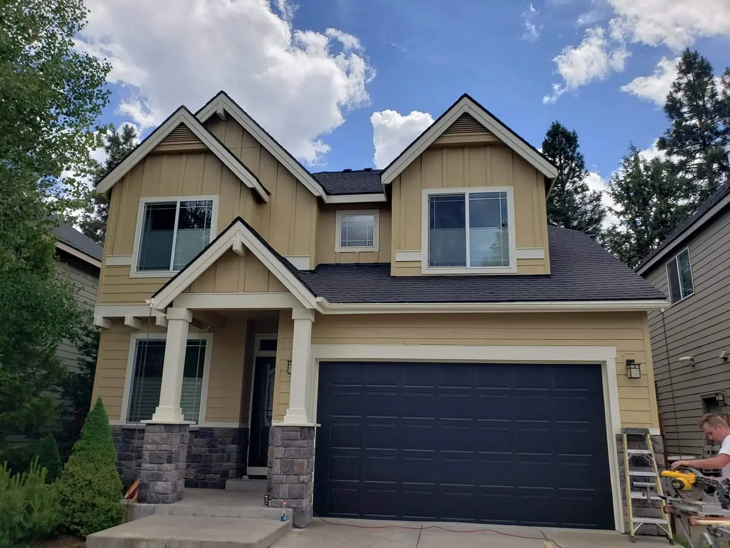 Front view of a Bend, OR craftsman home with tan siding, white trim, and a charcoal garage door.