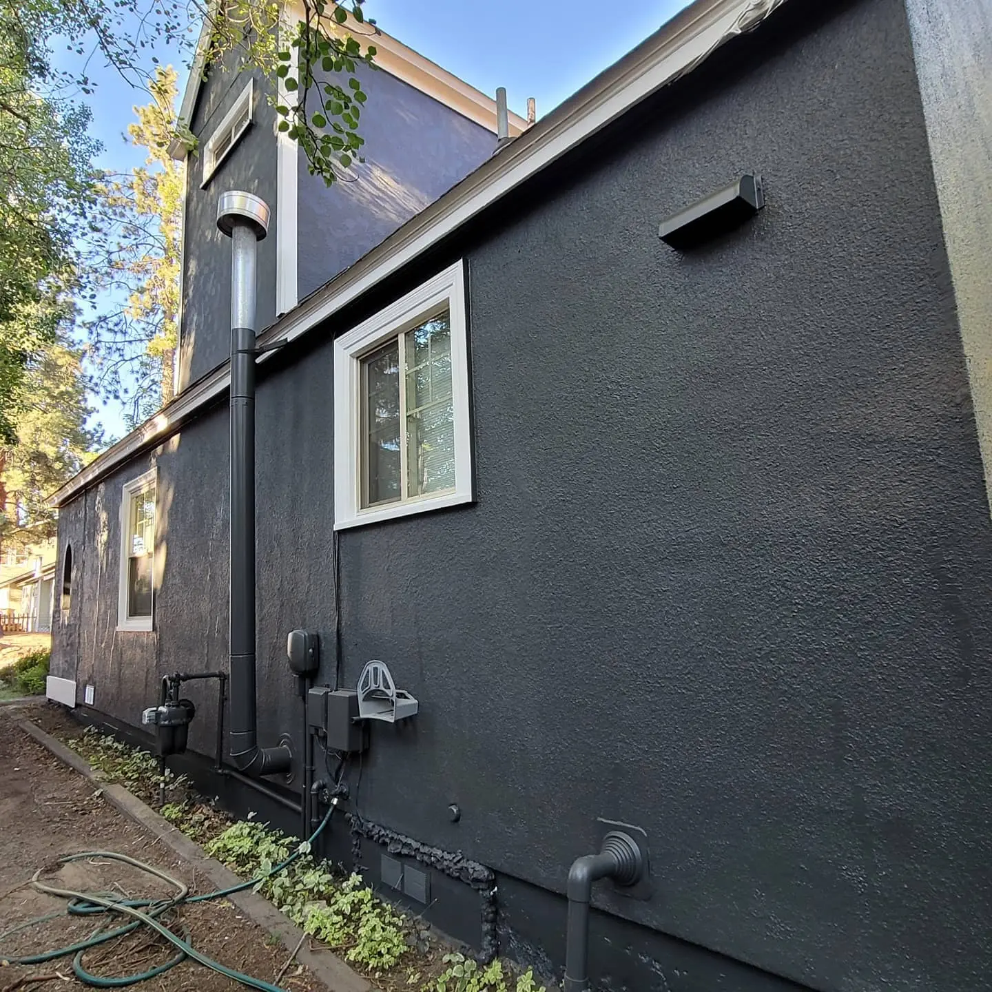 Side of a Bend home with dark charcoal stucco and pipes/vents painted to match the exterior wall for a clean look.