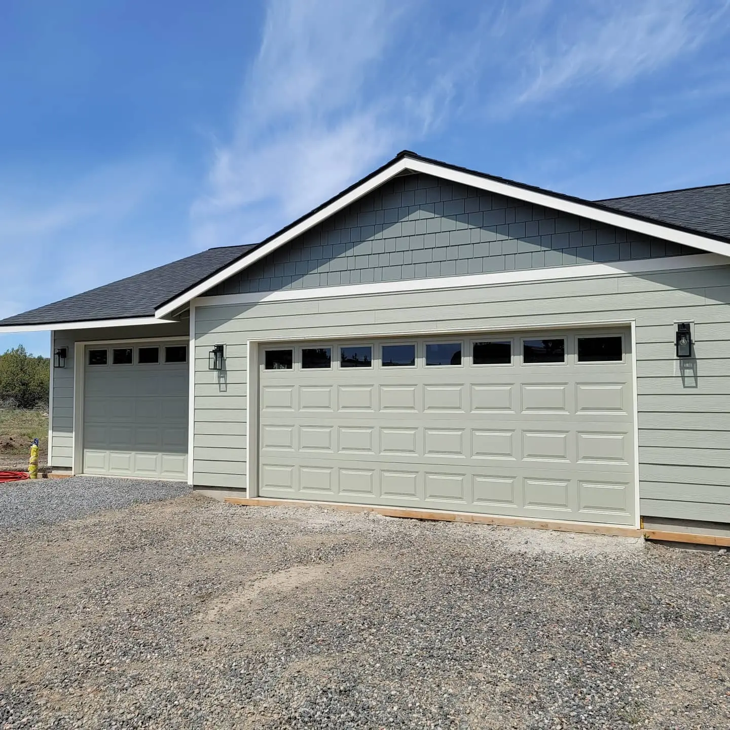 Two-car garage with freshly painted sage green doors and matching siding on a new Madras residential build.