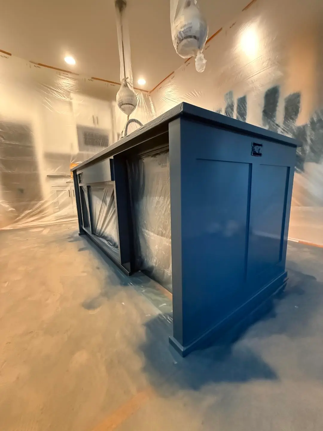 Professional masking and plastic sheeting setup for spray-painting a charcoal kitchen island.