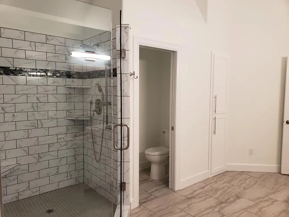 View of new marble-look floor tile and floor-to-ceiling white storage cabinets in a remodeled bathroom.