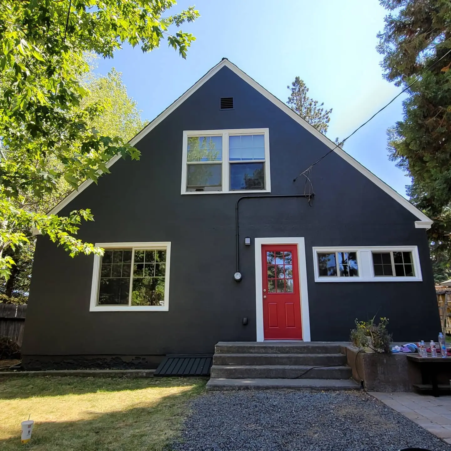 Rear exterior of a Bend home showcasing a modern color palette: charcoal grey stucco, white trim, and a red accent door.