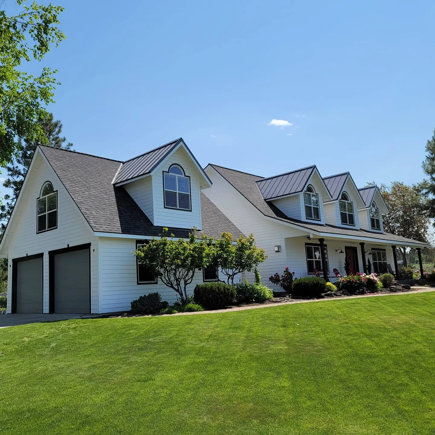 Side view of a large white farmhouse in Bend, OR, featuring black metal roof accents and black trim.