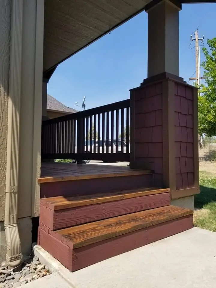 Side profile of a front porch featuring dark burgundy railings and natural wood steps.