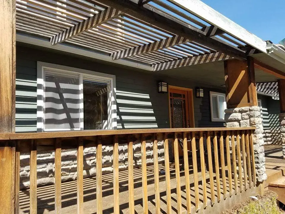 Close-up of a residential porch featuring fresh dark grey siding and a modern slatted wood pergola.