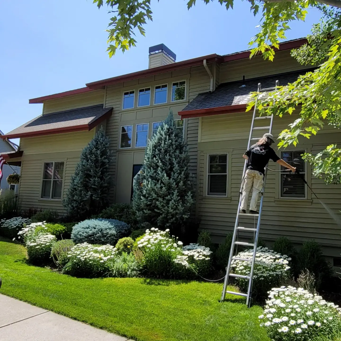 A professional painter in Sisters, OR, using a pressure washer to prep the home's exterior siding.