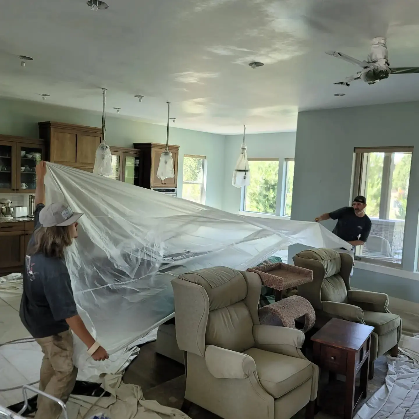 Professional painters in Redmond using plastic sheeting to carefully mask furniture before painting.