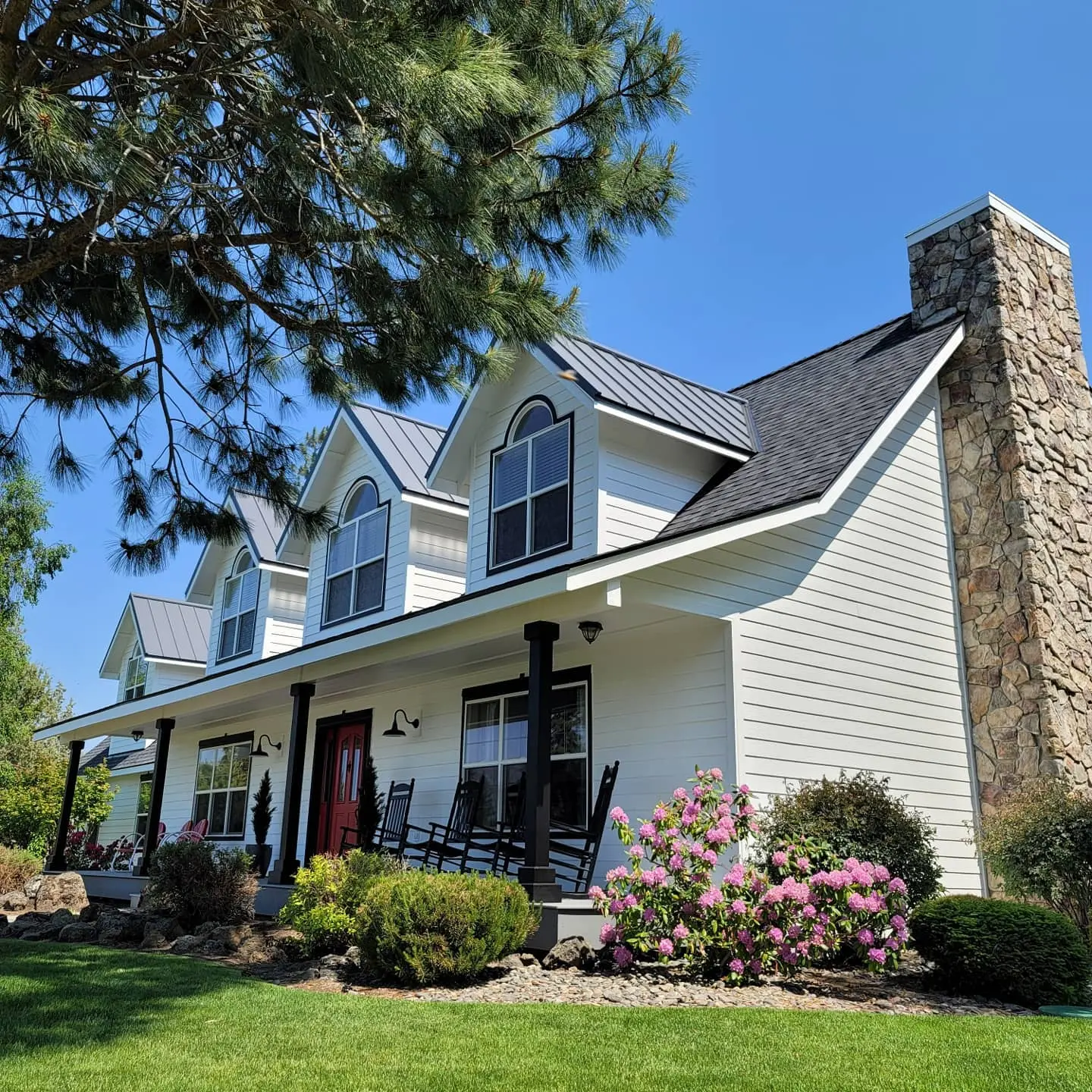 Front porch of a Bend home featuring white lap siding, stone chimney, and black architectural trim.