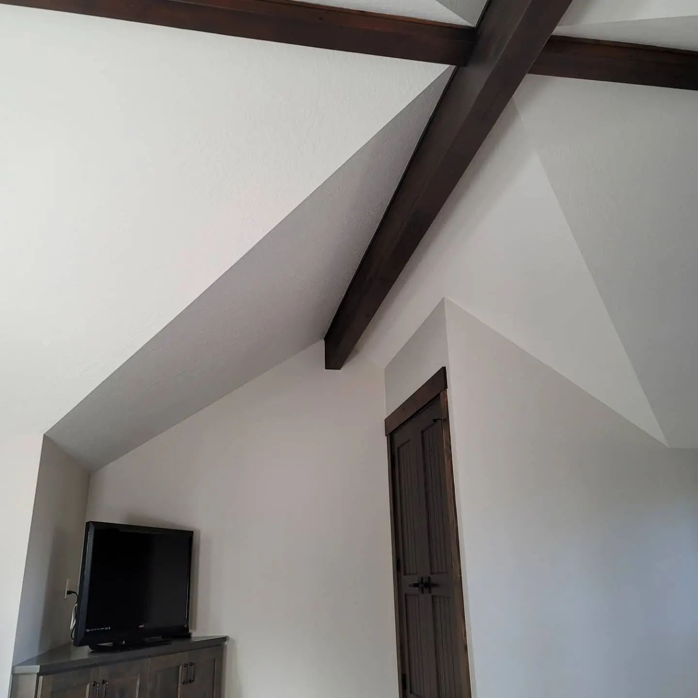 Master bedroom in Sunriver featuring vaulted peaks and dark stained beams against a crisp white ceiling finish.